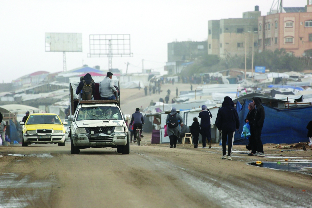 Displaced Palestinian walk past a vehicle carrying others west of Deir al-Balah city in the central Gaza Strip, on November 15, 2025 as a low-pressure system impacts the area. (Photo by Bashar TALEB / AFP)