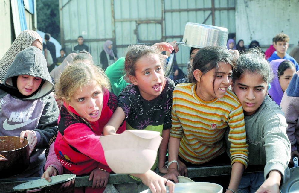 Displaced Palestinians wait for food at a shelter where families have been living, in Nuseirat, in the central Gaza Strip on Sunday. — AFP