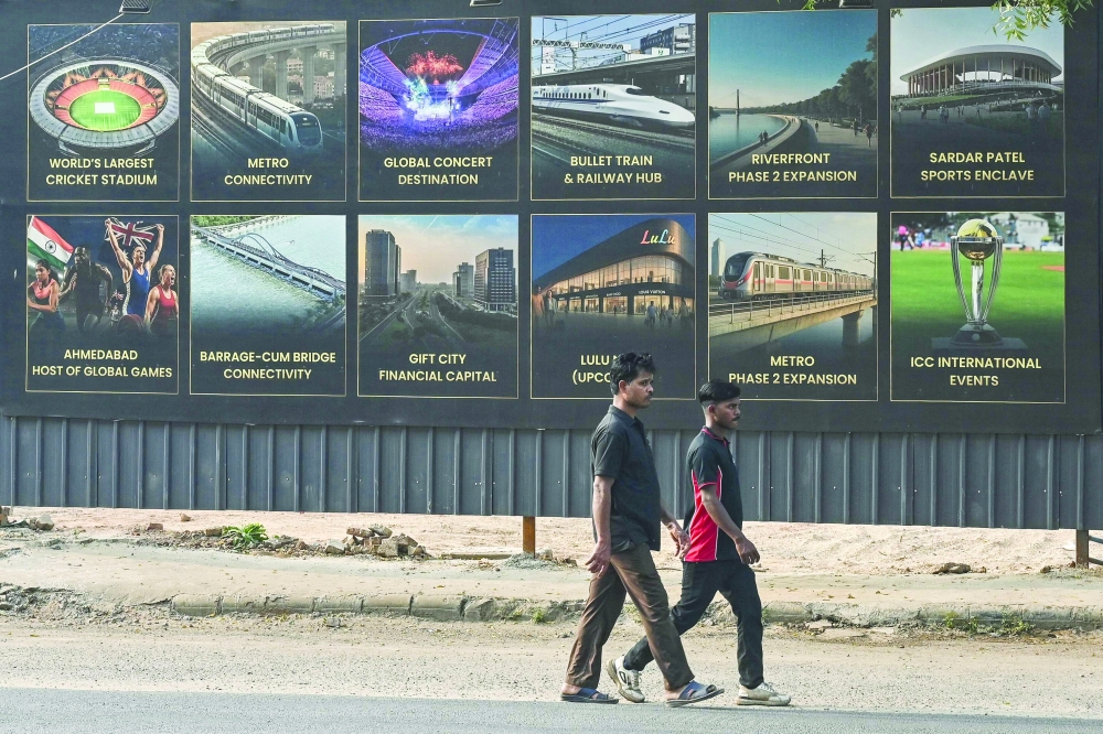 Men walk past a billboard featuring the ongoing infrastructure projects in Ahmedabad on November 26, 2025. (Photo by Shammi MEHRA / AFP)
