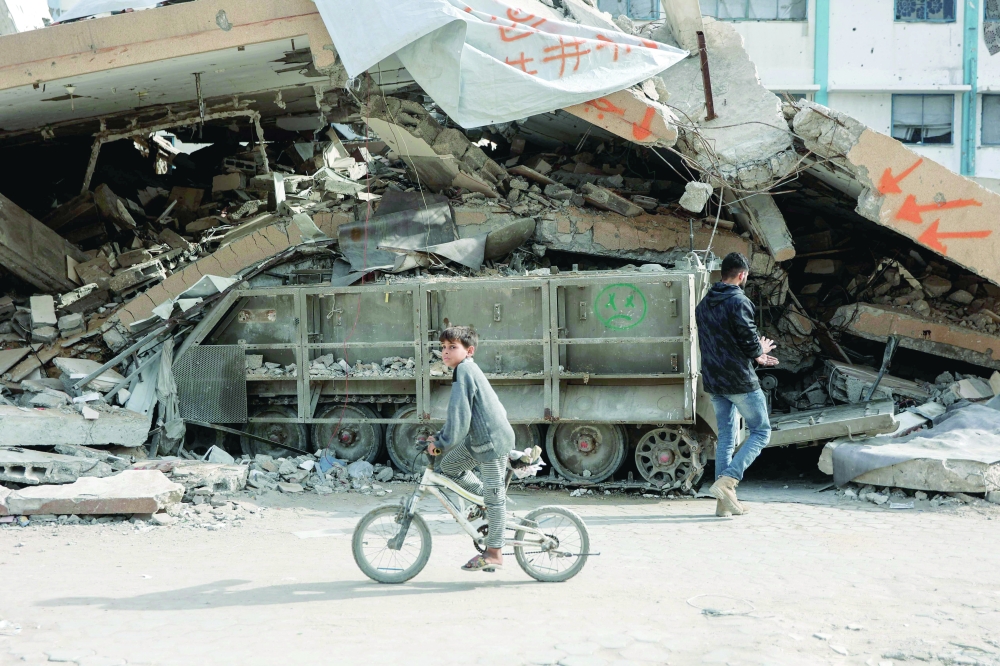 A Palestinian boy cycles past a converted Israeli military vehicle abandoned in Gaza. — AFP