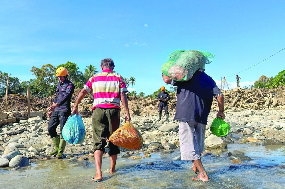 Villagers carrying food supplies walk through debris on a flooded road while being assisted by rescuers at Garoga village in South Tapanuli, North Sumatra. — AFP