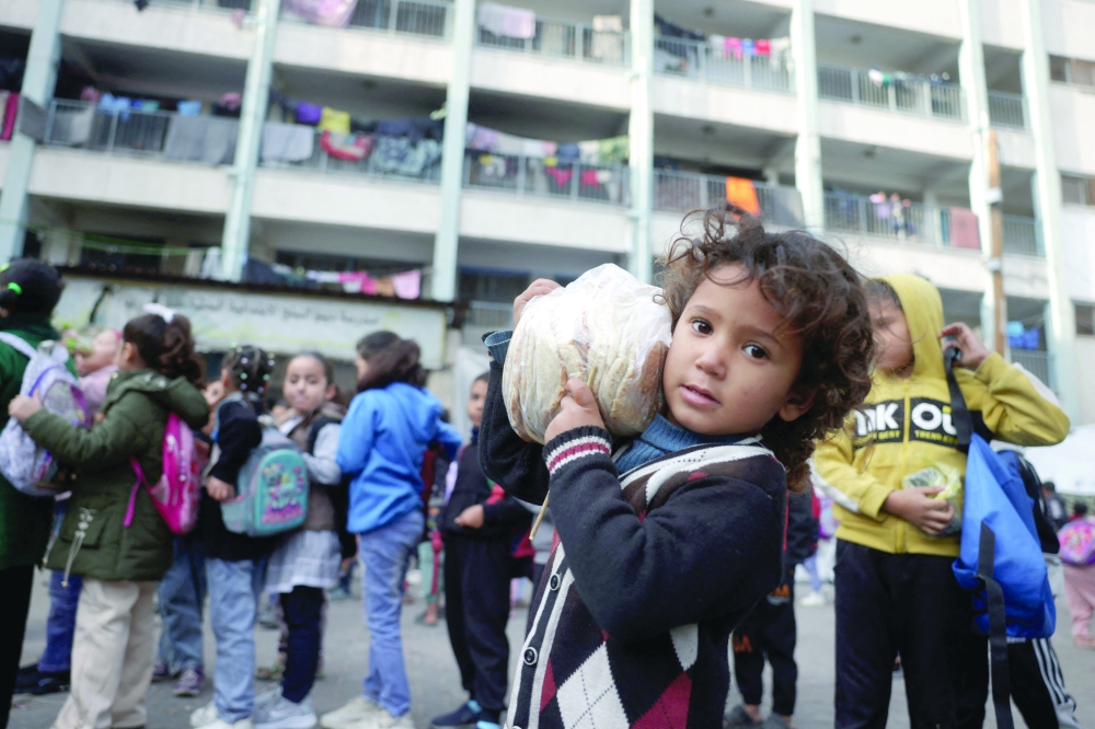 A Palestinian girl carries a bag of bread as others gather in the yard of the UNRWA Deir Al Balah Joint School, west of Deir Al Balah, in the central Gaza Strip on Saturday. — AFP