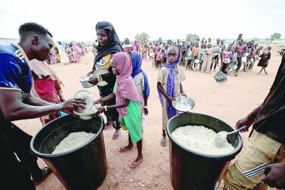 Sudanese people, who fled the conflict in Geneina in Sudan's Darfur region, receive rice portions from Red Cross volunteers in Ourang on the outskirts of Adre, Chad. - Reuters File 