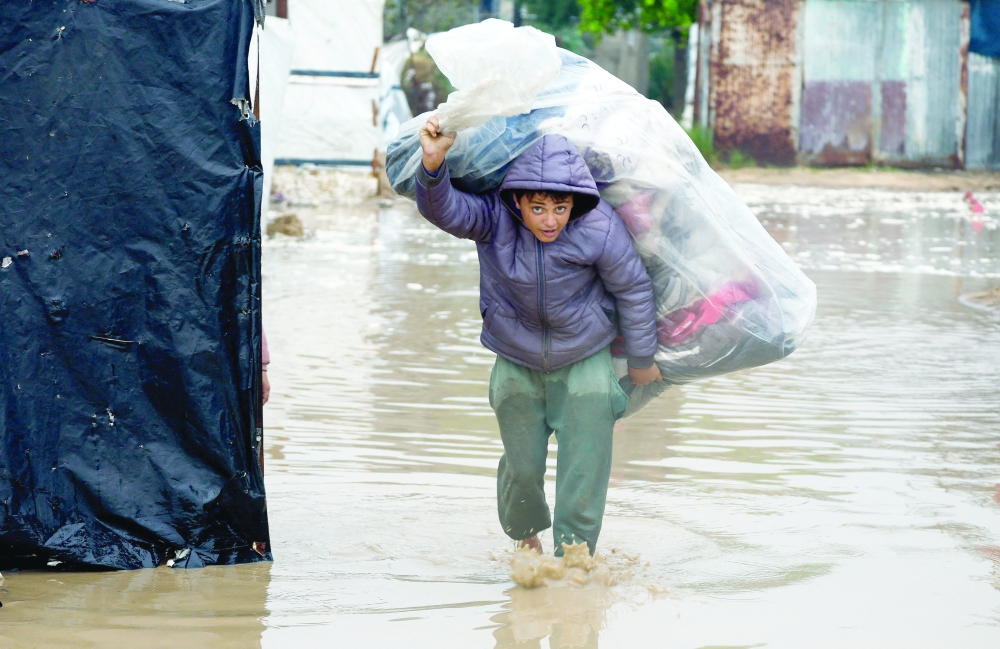 A Palestinian carries belongings in a tent camp on a rainy day in Nuseirat on Friday.—  Reuters