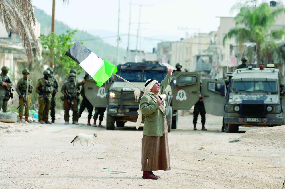 A Palestinian man holding the national flag gestures at the entrance of the Nur Shams refugee camp. — AFP