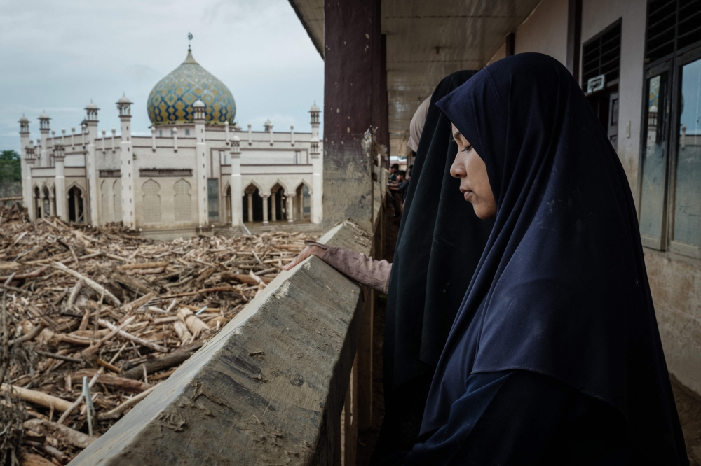 A middle school student who came with her teacher from Medang closes her eyes at a muddy corridor as piles of uprooted trees swept away by a flash flood remain at Darul Mukhlisin Islamic Boarding School and its attached mosque in Aceh Tamiang. — AFP