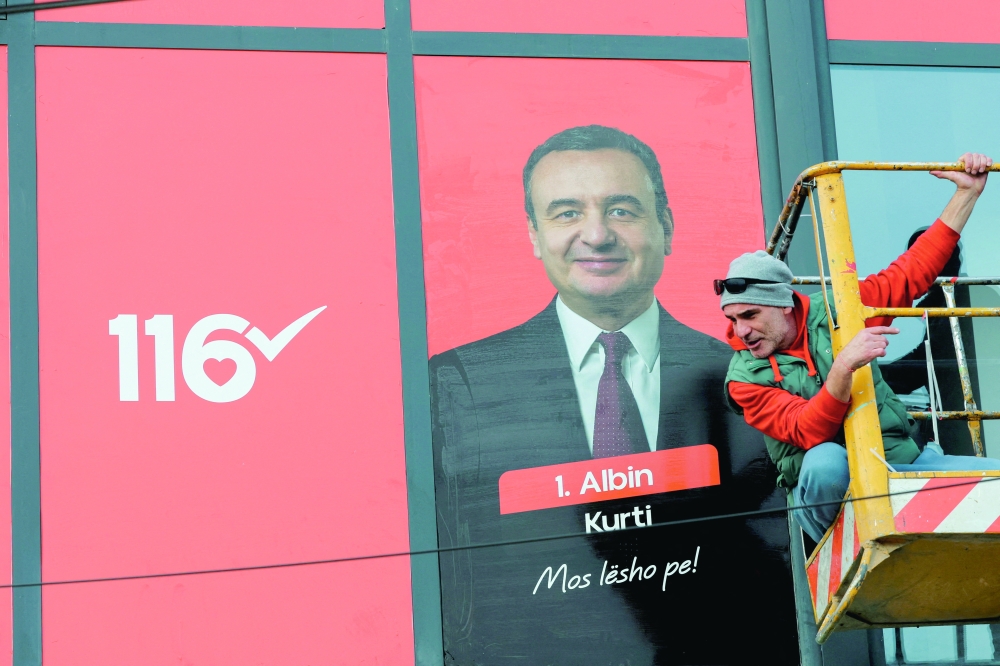 A worker looks down while putting up election campaign signs with a portrait of acting Prime Minister of Kosovo and Levizja Vetevendosje, in Pristina. — Reuters 