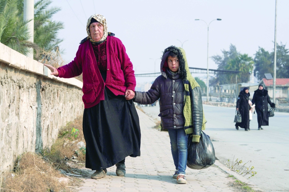 A boy walks with a woman, carrying his belongings, Aleppo. — Reuters