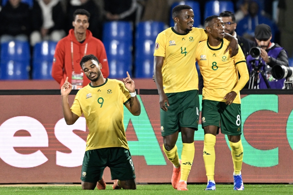 South Africa's forward #09 Lyle Foster (L) celebrates scoring his team's second goal next to South African midfielder #04 Teboho Mokoena (C) and South Africa's forward #08 Tshepang Moremi (R) during the Africa Cup of Nations (CAN) Group B football match between South Africa and Angola at Marrakesh Stadium in Marrakesh, Morocco on December 22, 2025.   (Photo by Khaled DESOUKI / AFP)