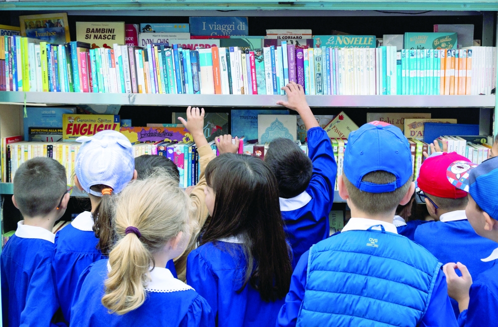 Children pick up books from the mobile library owned by Antonio La Cava, a retired schoolteacher known as 'Maestro', at the Racioppi elementary school in Italy. - Reuters 