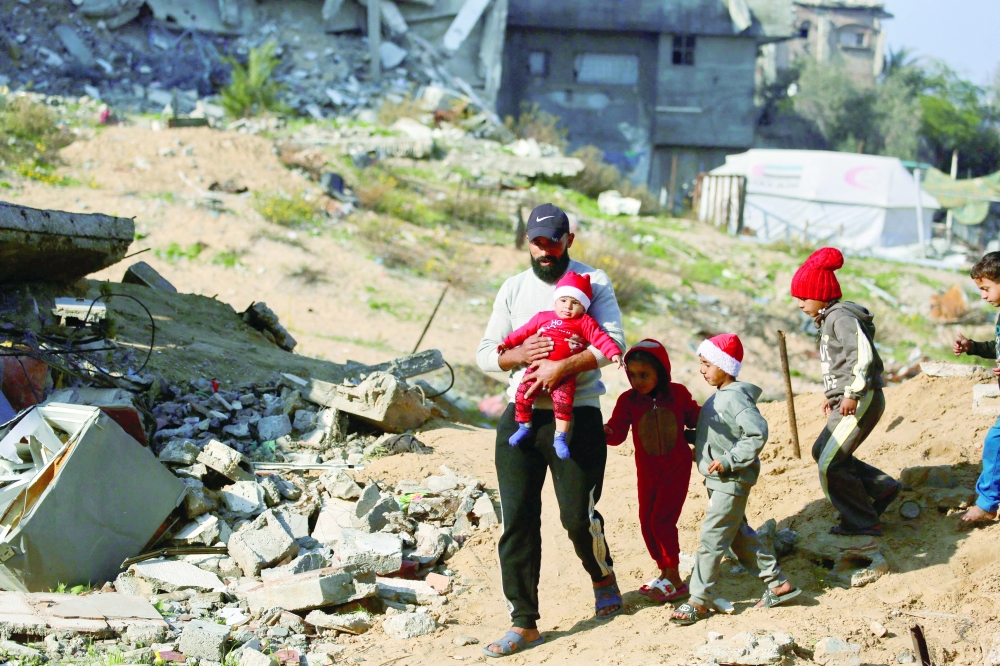 A Palestinian man walks with children next to the rubble of destroyed buildings, Gaza. — AFP