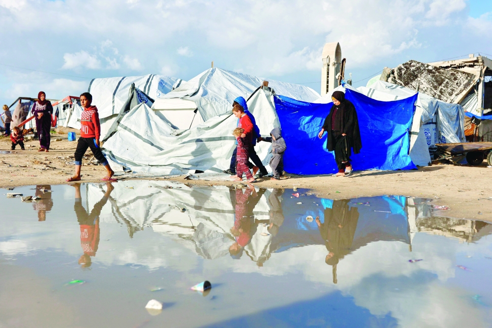 Displaced Palestinians walk past a large pool of rain water accumulated near tent shelters as the region experiences rain and cold winter conditions, in Gaza City an December 28, 2025. The majority of Gaza's 2.4 million people have been displaced, often multiple times, by the war that began with Hamas's attack on southern Israel on October 7, 2023. With many displaced living in tent camps, raising serious concerns over winter.  (Photo by Omar AL-QATTAA / AFP)
