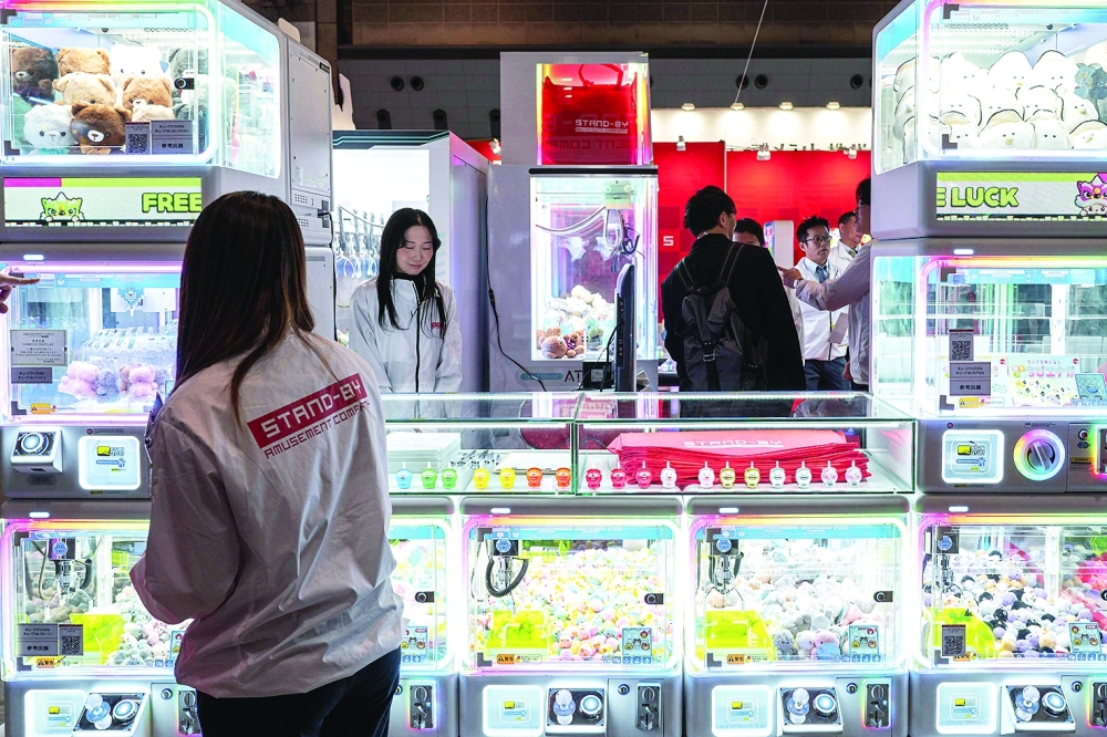 This picture taken on November 14, 2025 shows staff members of Stand-by Amusement Company standing by claw crane game machines during the Amusement Expo 2025 in Tokyo. As school and work wraps up, crowds gradually fill Tokyo's many bustling arcade halls —- not to battle it out in fighting games, but to snag plush toys from claw machines. - To go with 'JAPAN-ANIMATION-GAME-ARCADE, FOCUS' by Mathias Cena

