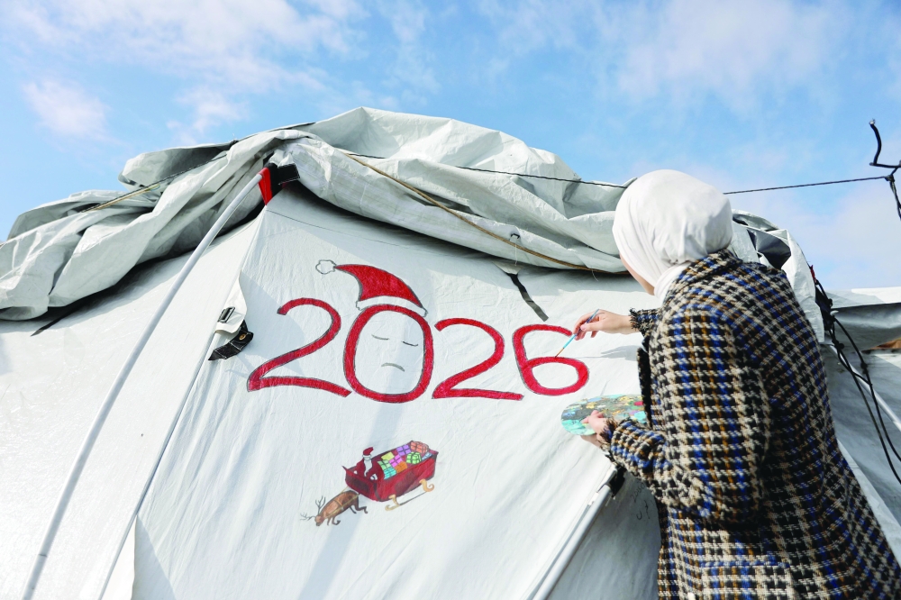 Fifteen-year-old displaced Palestinian Sarah Saada, who fled Beit Lahia in the northern Gaza Strip during Israeli bombardment, paints on her tent in Gaza City on Tuesday. — AFP