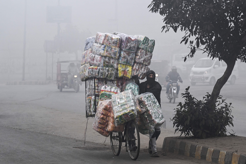 ndor with his face covered in cloth carries food items on a bicycle along a street amid dense smog in Lahore on December 30, 2025.  (Photo by Arif ALI / AFP)