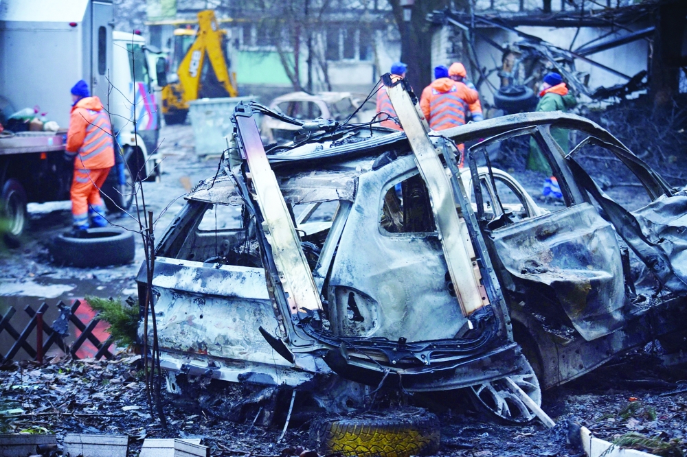 Communal workers clean debris in the courtyard of a damaged residential building next to destroyed cars following a drone attack in Dnipro. - AFP