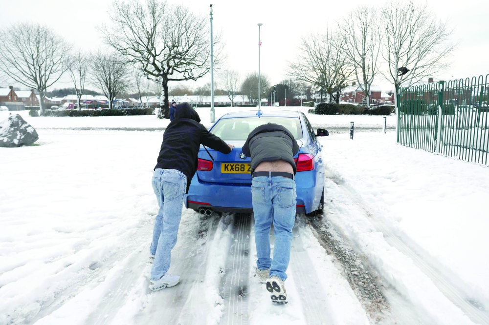 Men push a car off a snow-covered car park in Coalville, central England. — AFP