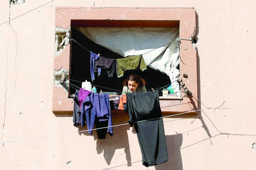 A displaced Palestinian girl looks out of the window of a building damaged during earlier Israeli military strikes, in Gaza City on January 11, 2026. The majority of Gaza's 2.4 million people have been displaced, often multiple times, by the war that began with Hamas's attack on southern Israel on October 7, 2023. With displaced families living in tented camps, a serious concerns has been raised over their living conditions. (Photo by Omar AL-QATTAA / AFP)
