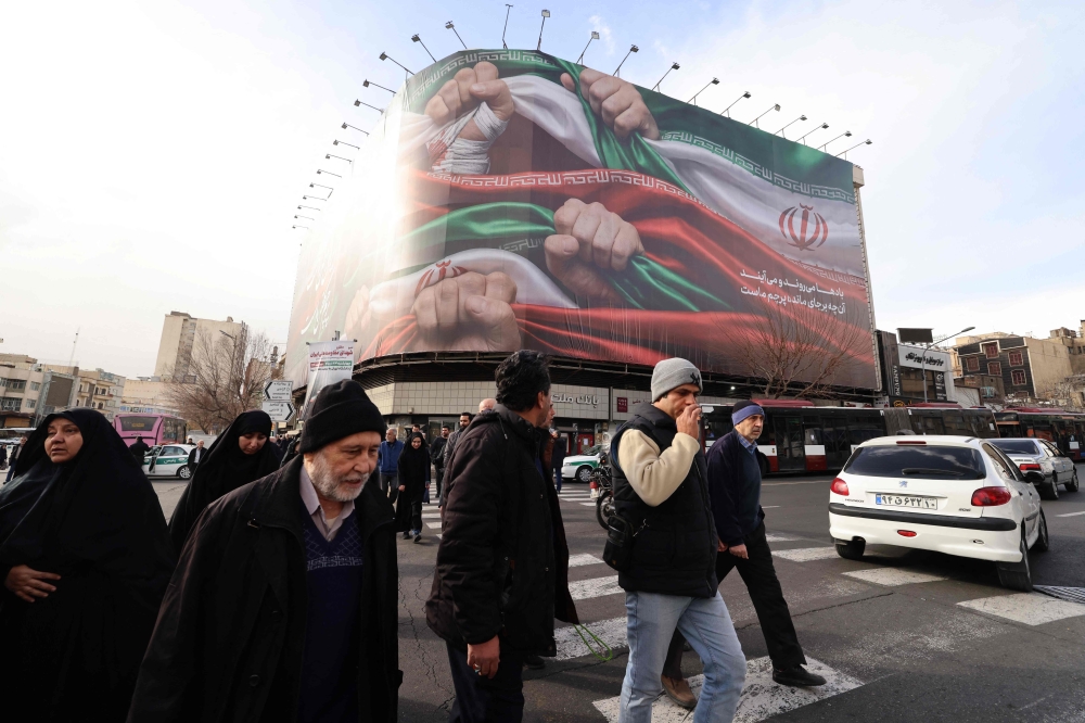 People walk past a large patriotic banner depicting the Iranian flag on Enghelab Square in Tehran on January 14, 2026.