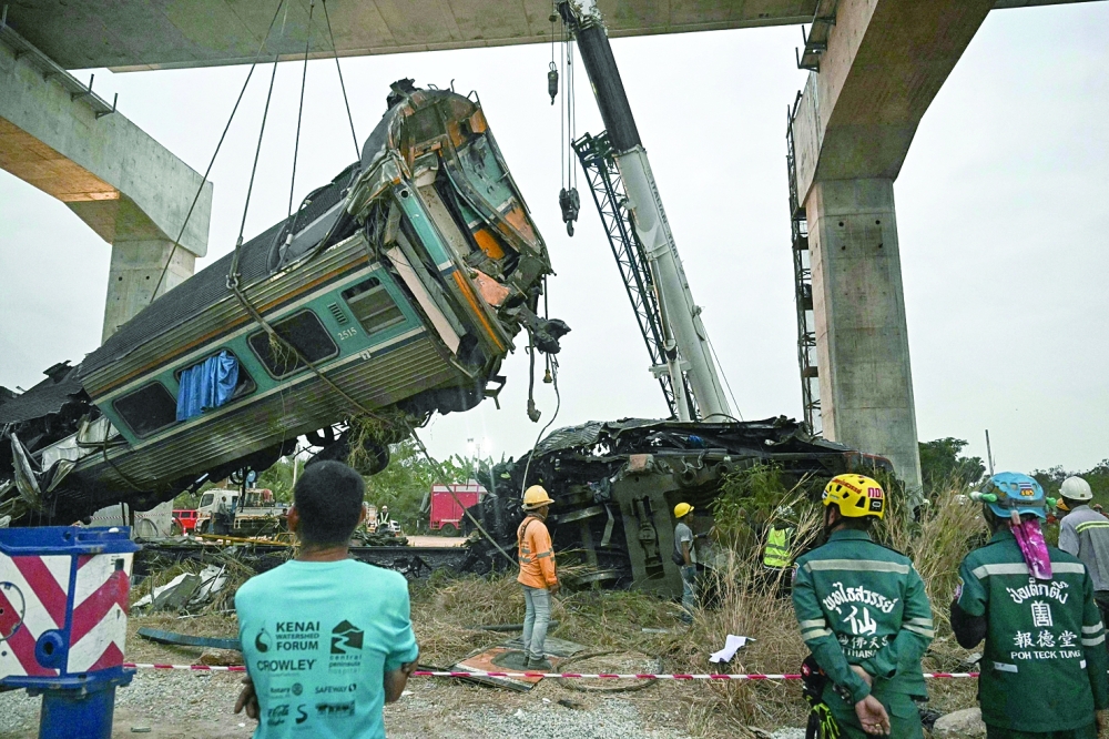 Recovery workers watch as a carriage of a train that crashed when a construction crane collapsed is lifted off the tracks in Thailand's Nakhon Ratchasima province on January 14, 2026. A crane at a China-backed high-speed rail project in Thailand collapsed onto a passenger train on January 14 and caused it to derail, killing at least 28 people and injuring dozens more, authorities said.
 (Photo by Lillian SUWANRUMPHA / AFP)
