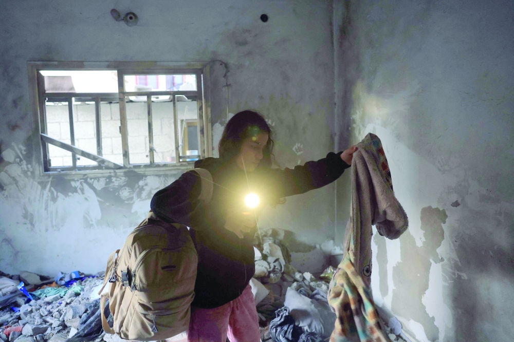 A woman uses the torch light on her mobile phone to collect items of clothing from under the debris in a room, after an Israeli military attack on the home of the Al Houli family, in which four people were reportedly killed, west of Deir Al Balah, in the central Gaza Strip on Friday. — AFP