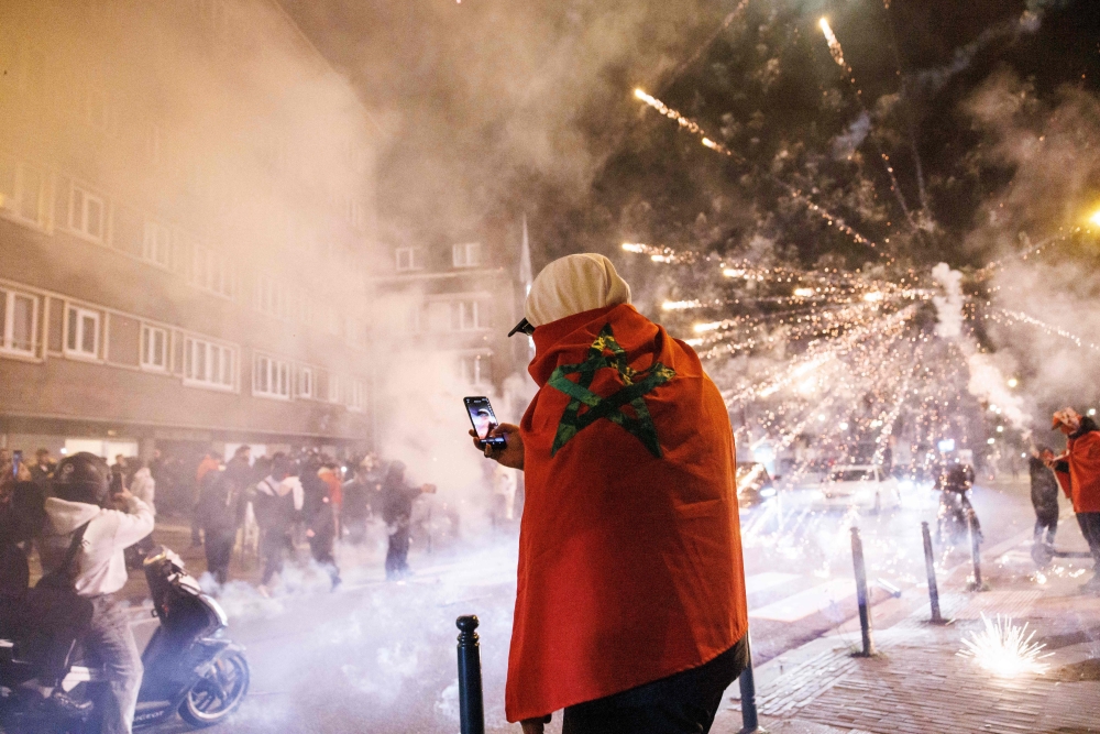 A supporter with a Moroccan national stands near fireworks going off in a street in Brussels 