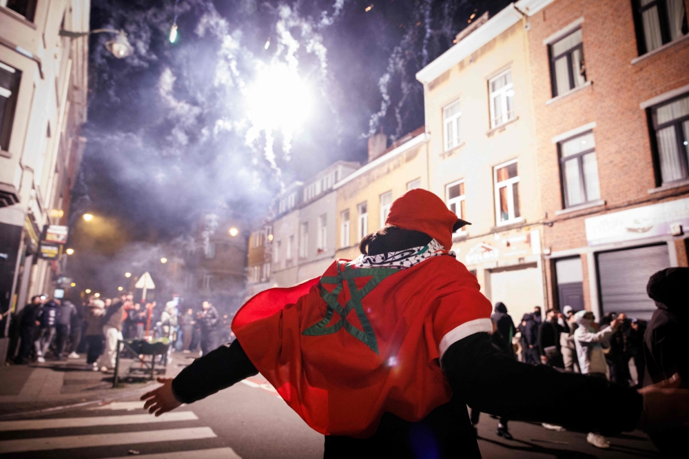 A supporter with a Moroccan national flag gestures near fireworks going off in a street in Brussels 