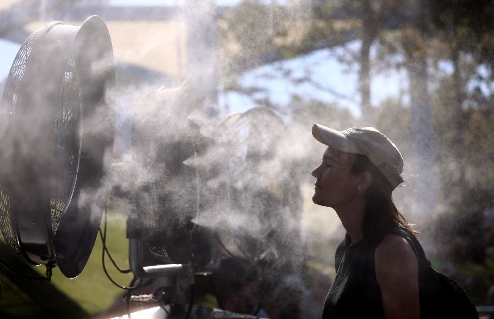  A woman cools herself down in front of a mist fan during the day's play  