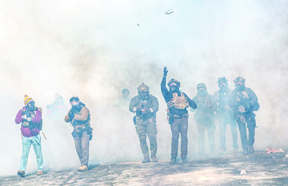 A federal agent lobs a teargas canister towards protesters, in Minneapolis. — AFP