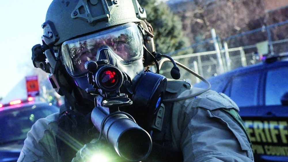 A law enforcement member holds a weapon as they stand guard while people protest outside the Bishop Henry Whipple Federal Building