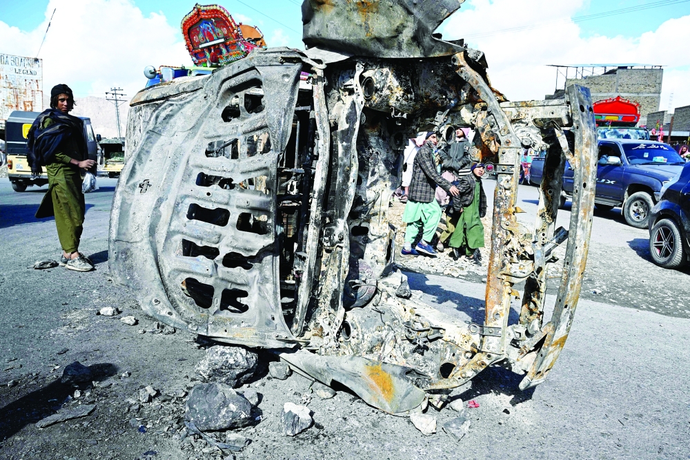 Bystanders walk past a burnt vehicle along a road on the outskirts of Quetta, a day after an attack by separatists. - AFP