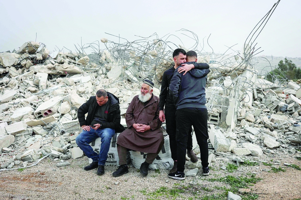 Palestinian men sit on the rubble as others console each other, in Ramallah. — AFP