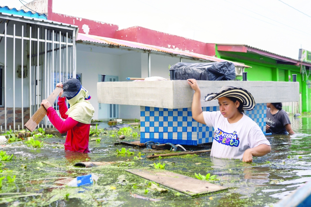 People carry belongings on a flooded street in Monteria, Colombia on February 9, 2026.  At least 13 deaths were reported this week in different parts of Colombia due to the intense rains battering the country, which are unusual for this time of year, according to a report on February 8, 2026, based on official information. (Photo by STRINGER / AFP)
