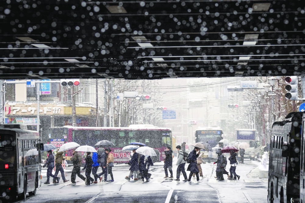 People cross a street during a snowfall in Tokyo on February 8, 2026. (Photo by Yuichi YAMAZAKI / AFP)
