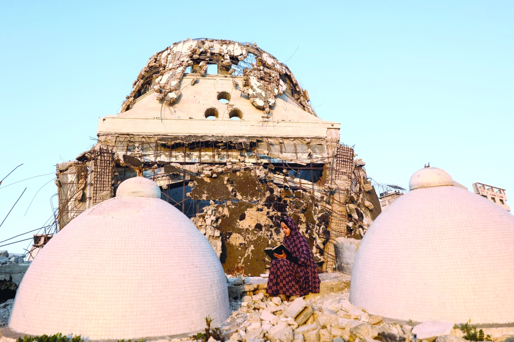 
A Palestinian sits in the debris of the Al Hasayna Mosque as she recites from a copy of the Quran, during the holy month of Ramadhan in western Gaza City on Sunday. — AFP 