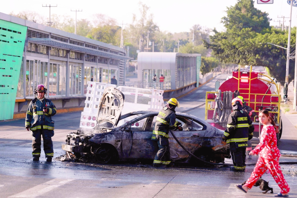 Firefighters extinguish a burning vehicle set on fire by organised crime groups, Mexico. — AFP