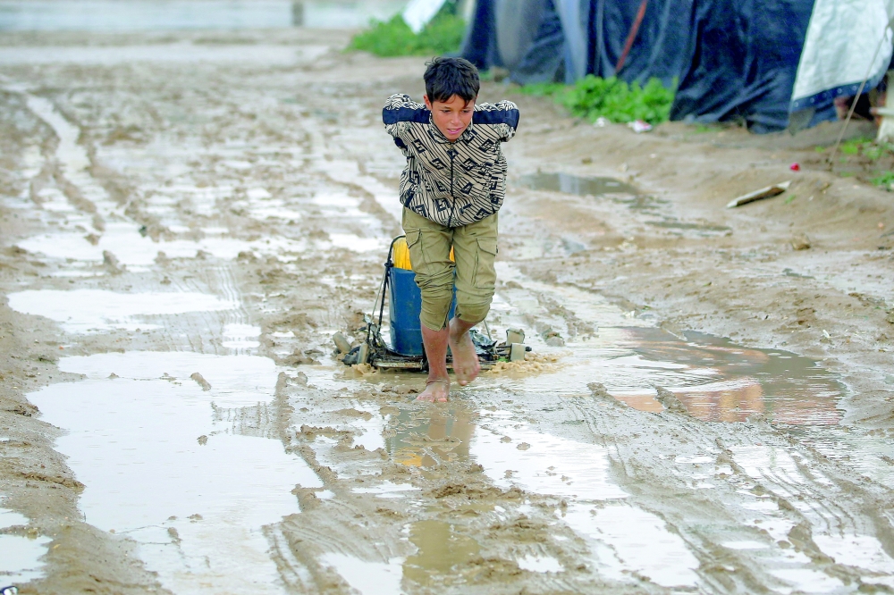 A boy pulls a water container along a muddy road after heavy rain at the Bureij camp for Palestinian refugees in the central Gaza Strip on Tuesday. - AFP