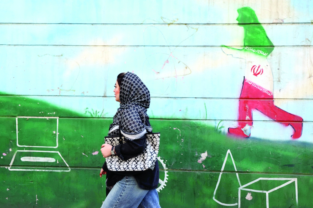A woman walks past a wall painting in the colours of the Iranian flag in Tehran on Wednesday. - AFP