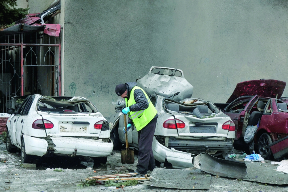 A municipal worker removes debris next to damaged cars outside an apartment building hit by a Russian drone strike in Kharkiv, Ukraine. - Reuters 