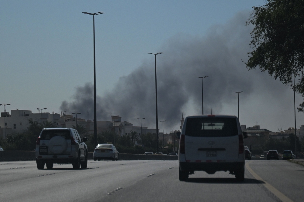 otorists drive along a street as smoke rises from a reported Iranian strike in the area where the US Embassy is located in Kuwait City on March 2, 2026. 