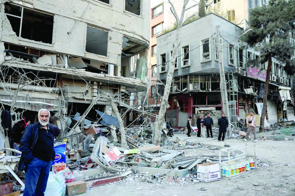 Residents stand on a street beside damaged residential buildings near Niloufar square in Tehran during the ongoing joint US-Israeli military campaign on Iran on Monday. — AFP