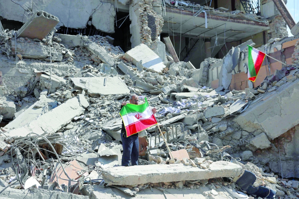 A man holds an Iranian flag amid the debris of a destroyed building following airstrikes in central Tehran. — AFP