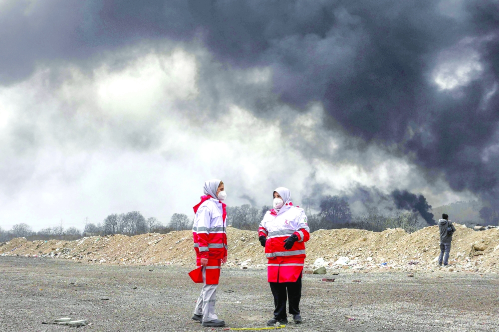 Women members of Iran's Red Crescent society stand near smoke plumes, Tehran. — AFP