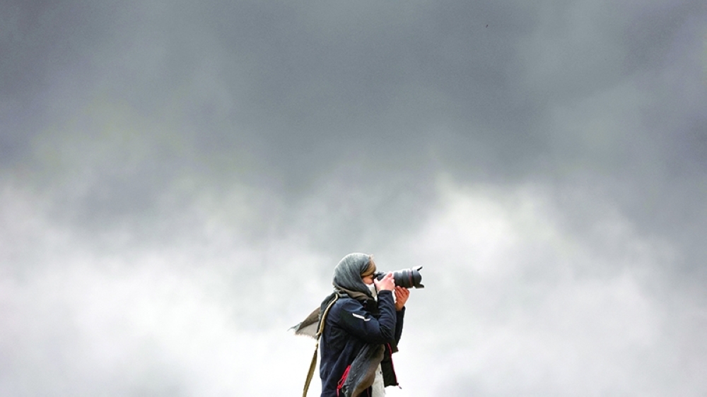 A photographer takes pictures as smoke rises after a reported strike on Shahran fuel tanks in Tehran, Iran, on Sunday. - Reuters
