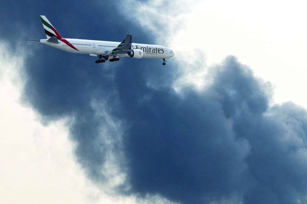 An Emirates aircraft prepares for landing as a smoke plume rises, at Dubai International Airport. — AFP