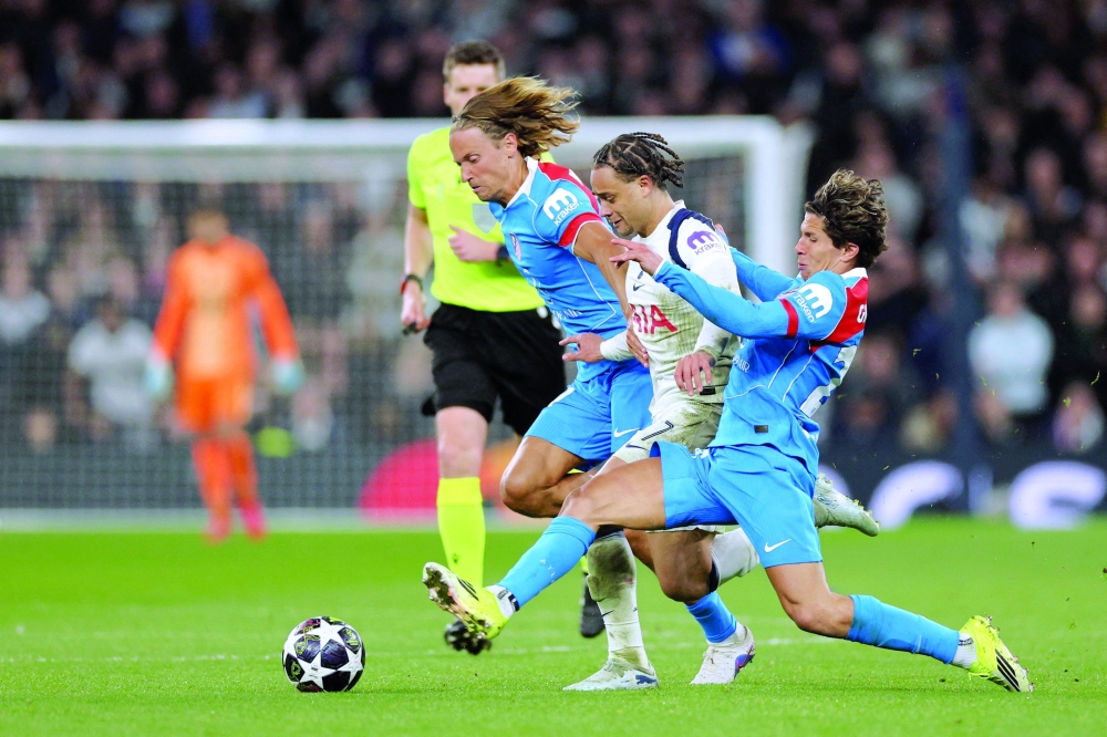 Tottenham Hotspur's Dutch midfielder #07 Xavi Simons is tackled by Atletico Madrid's Argentine forward #20 Giuliano Simeone (R) and Atletico Madrid's Spanish midfielder #14 Marcos Llorente (L) during the UEFA Champions League round of 16 second leg football match between Tottenham Hotspur and Atletico Madrid at the Tottenham Hotspur Stadium in London, on March 18, 2026.  (Photo by Adrian Dennis / AFP)
