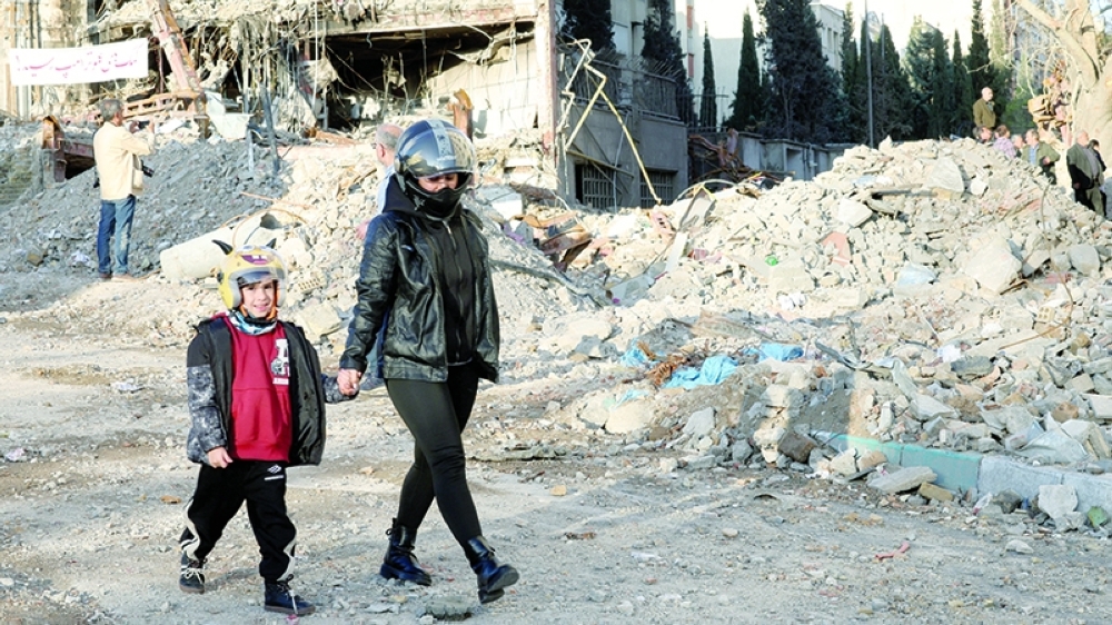 A mother and son walk near a building destroyed in a strike in Tehran, Iran, on Saturday. - Reuters