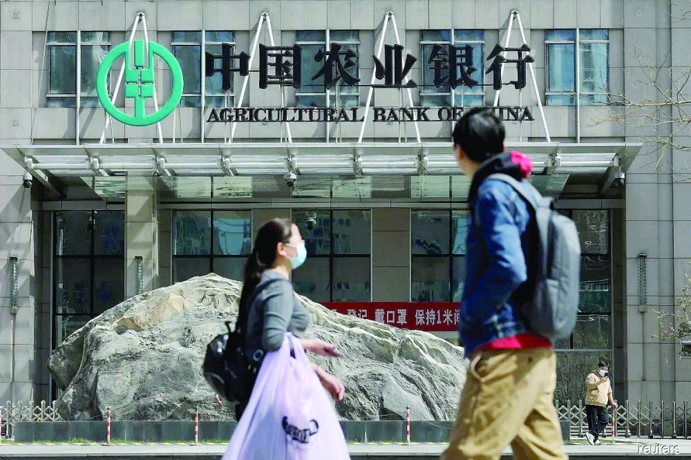 People walk past an office building of Agricultural Bank of China, in Beijing, China. — Reuters