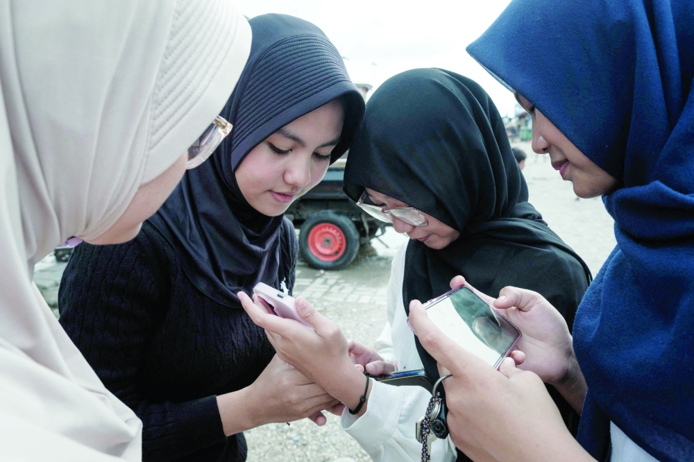 Girls use their smartphones on a street in Jakarta. — AFP