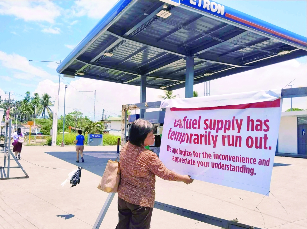 A pedestrian reads a sign at a petrol station in Tacloban City, Leyte province, central Philippines on March 30, 2026.  The Philippines' sole oil refinery has secured nearly 2.5 million barrels of Russian crude out of "extreme necessity", a stock exchange filing revealed on March 30, as the country seeks to replenish fast-dwindling fuel reserves. (Photo by Marlon TANO / AFP)
